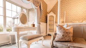 A room with a large window, a vanity with a mirror, a chaise lounge, and a patterned wallpaper. - Plas Dinas Country House (Caernarfon)