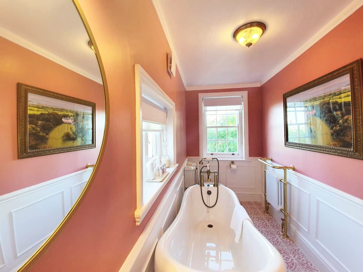 A bathroom with a freestanding bathtub, a window, and two framed pictures on the walls.