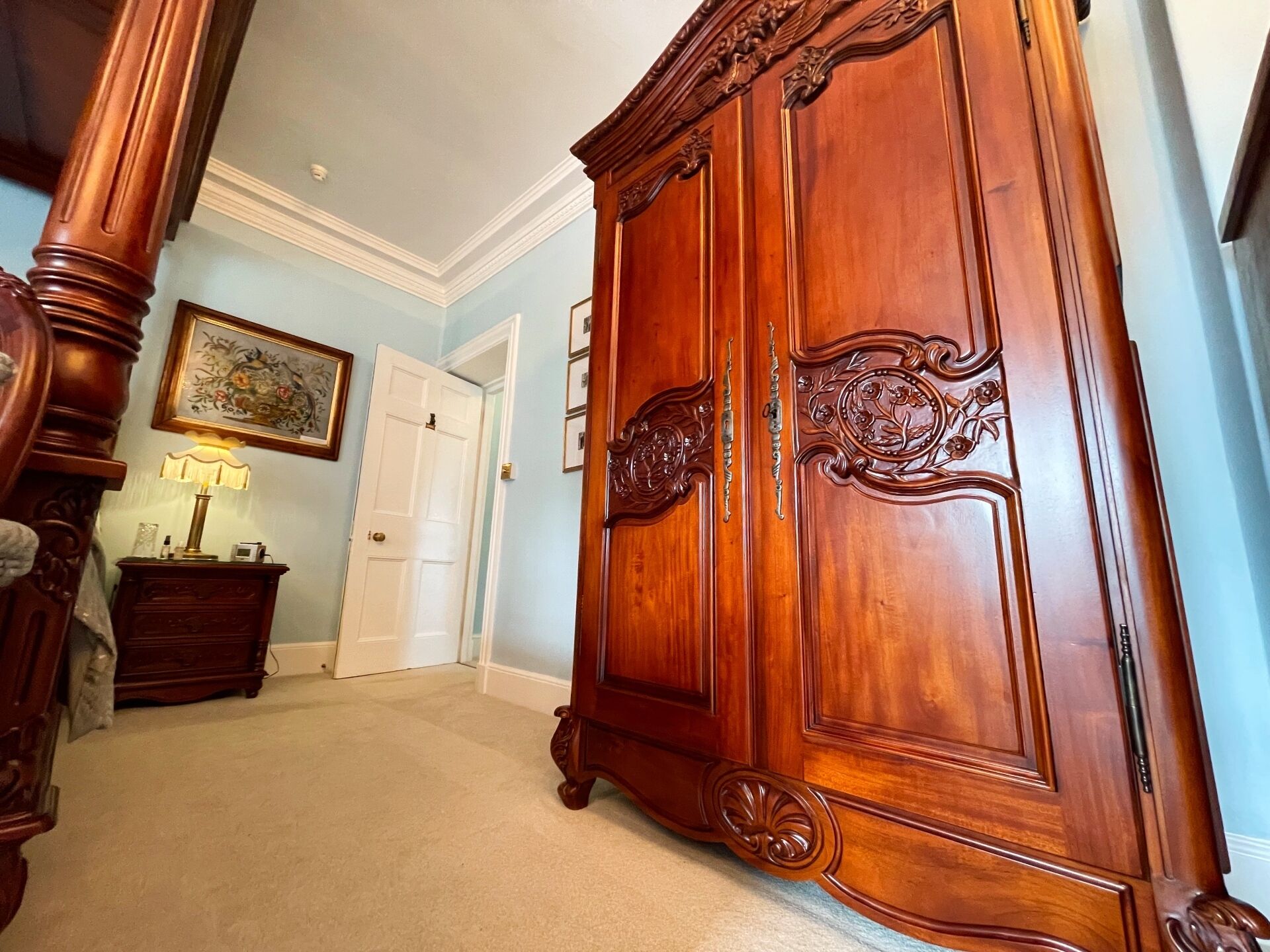 A hallway with a large wooden wardrobe, a door, a lamp, and a framed picture on the wall.
