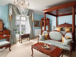 A traditional bedroom with a four-poster bed, a wooden dresser, a chair, and a table with a tray.
