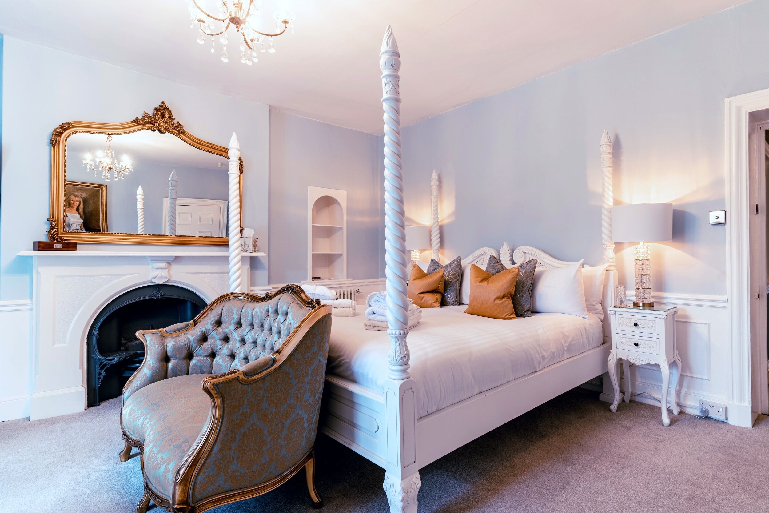 Un dormitorio con cama con dosel, un espejo grande, un candelabro y una chimenea.