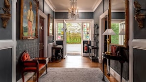 A grand hallway with a chandelier, framed paintings, and a red chair. - Plas Dinas Country House (Caernarfon)
