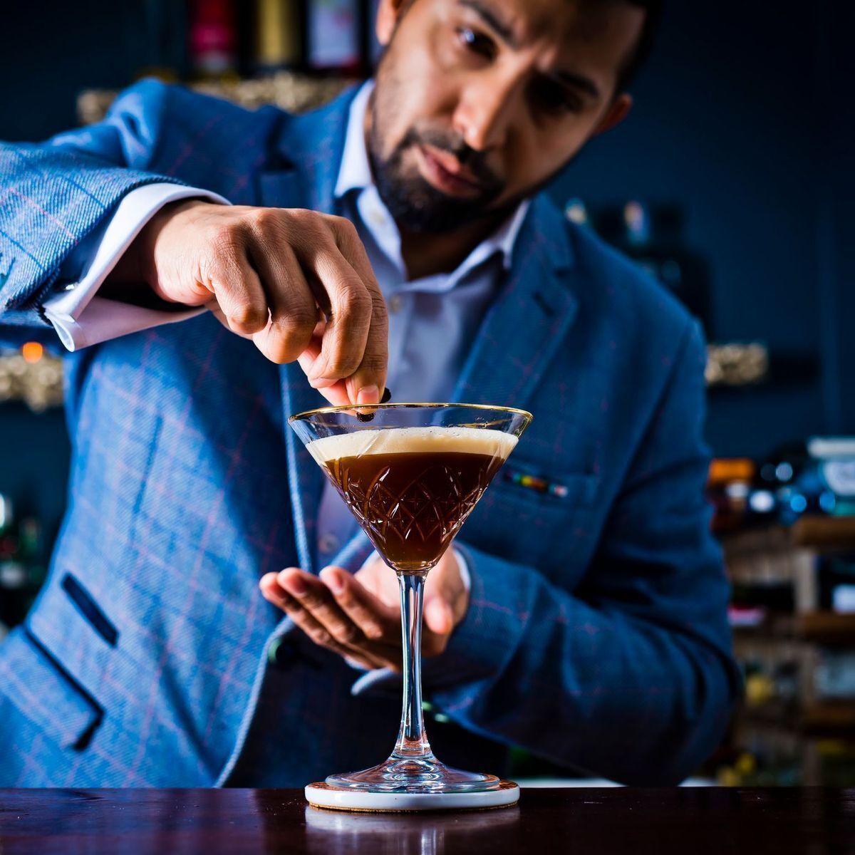 A person in a blue checkered suit pouring a drink into a martini glass.