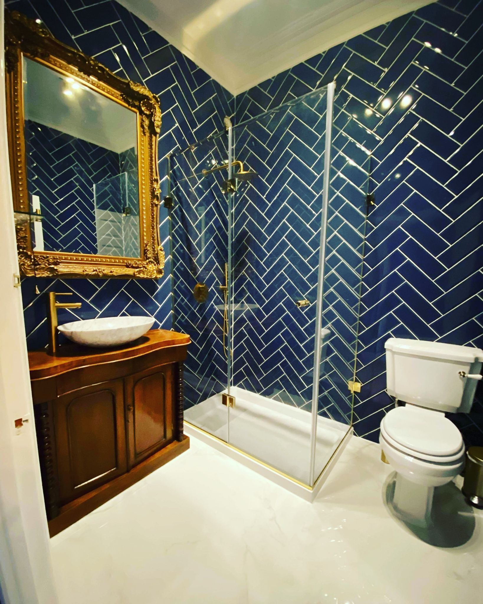 Un baño con suelo de baldosas en espiga, ducha separada, tocador de madera con lavabo e inodoro.