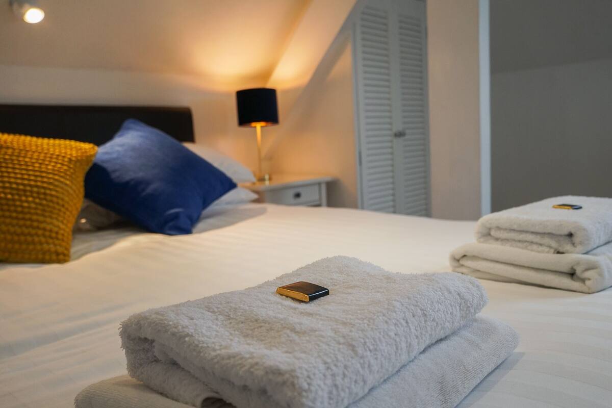 A neatly made bed with white towels and a small electronic device on top.