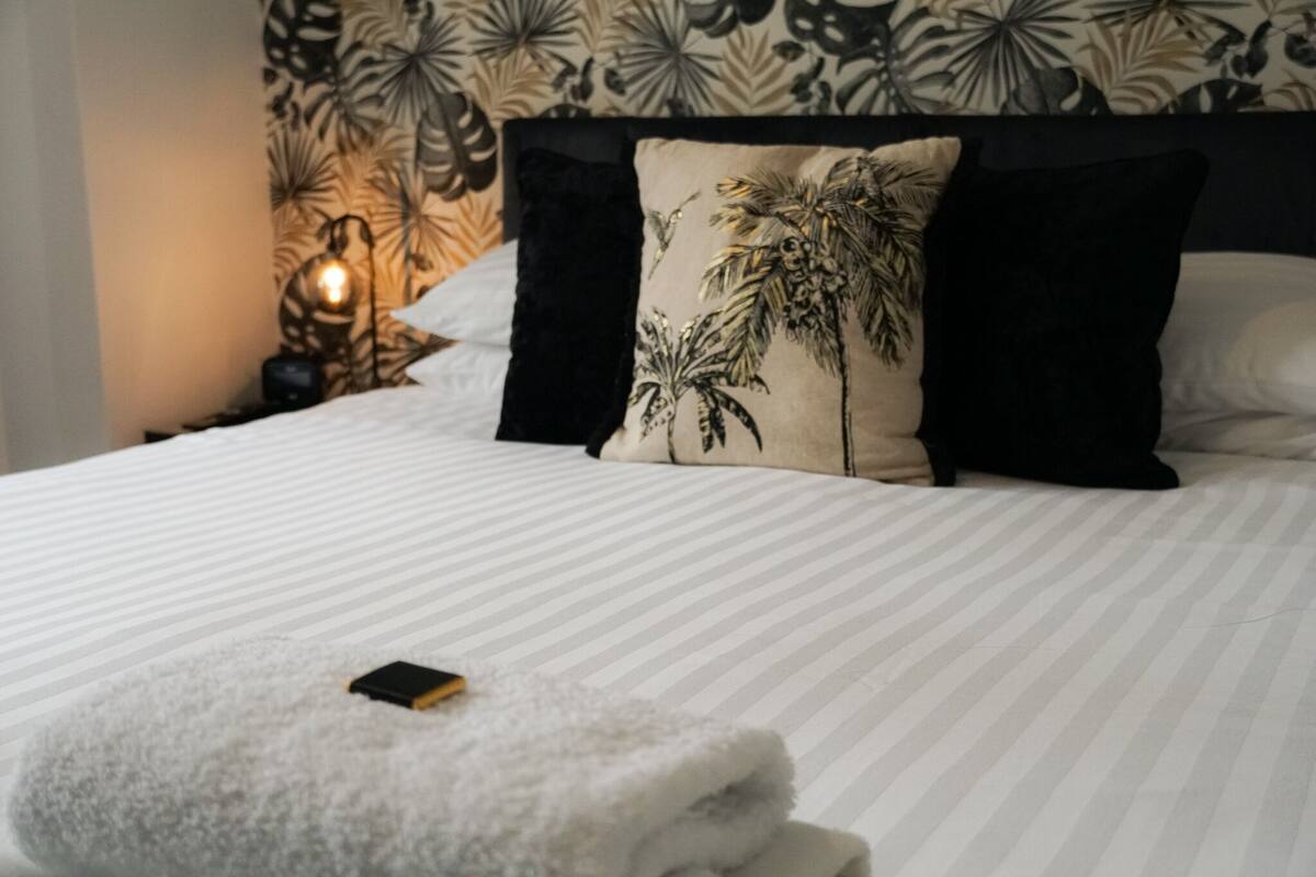 A neatly made bed with striped bedding, a decorative pillow with palm tree design, and a bedside lamp.