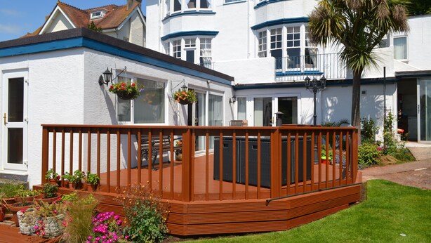 A white building with blue trim, a wooden deck, and potted plants. - The Sandpiper Guest House (Torquay)