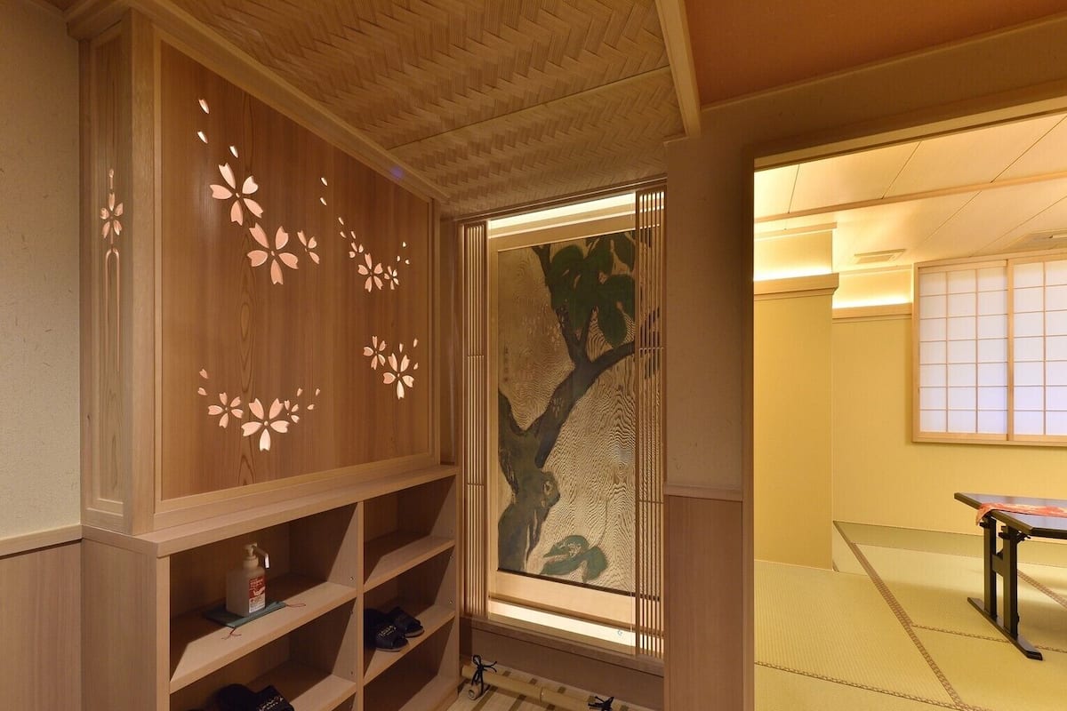 A traditional Japanese room with tatami flooring, a sliding door with a tree design, and a wooden cabinet with shelves.