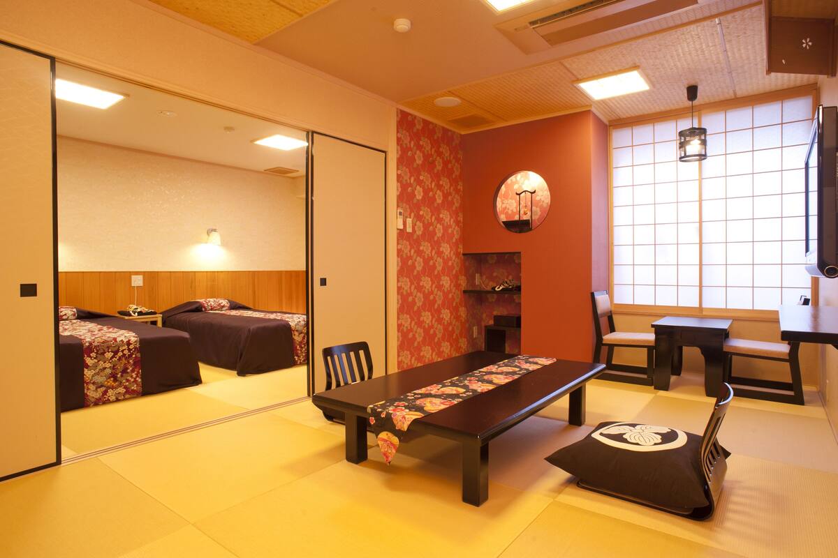 A traditional Japanese-style room with tatami flooring, a low table, and a bed with a floral bedspread.