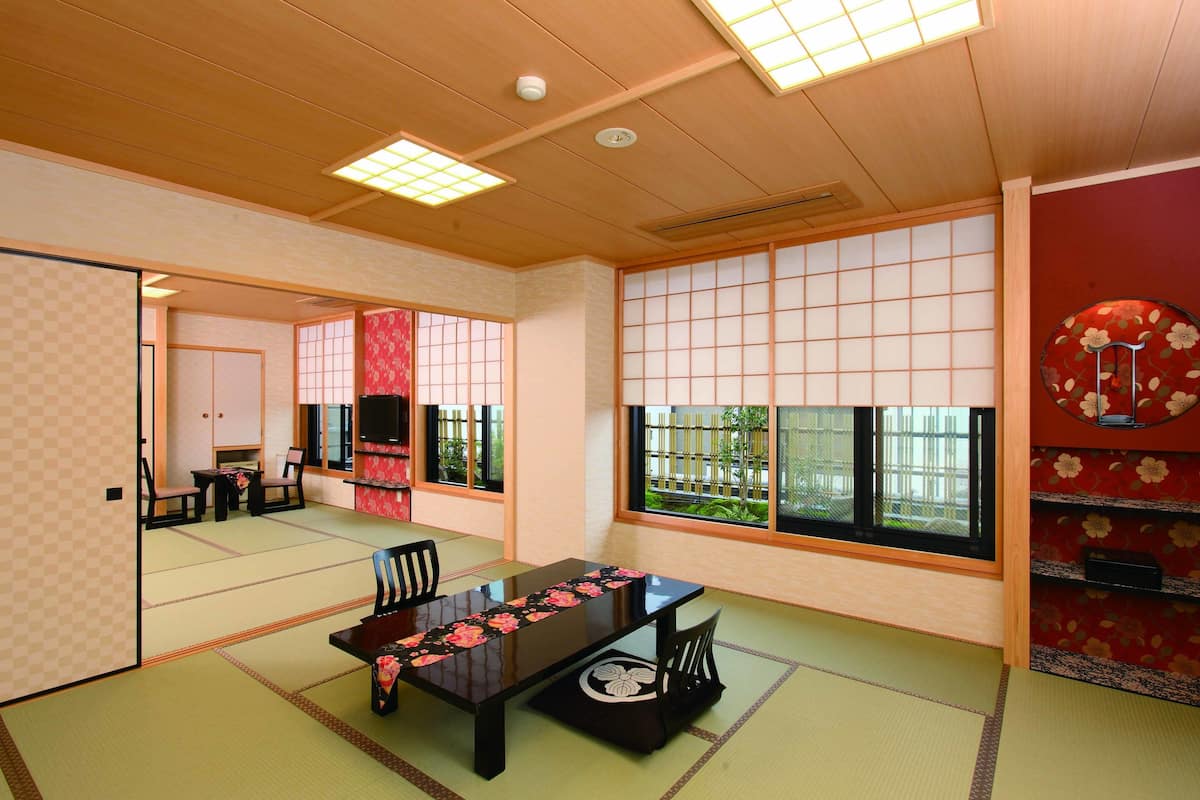 A traditional Japanese room with tatami flooring, a low table with a floral table runner, sliding doors, and a view through large windows.