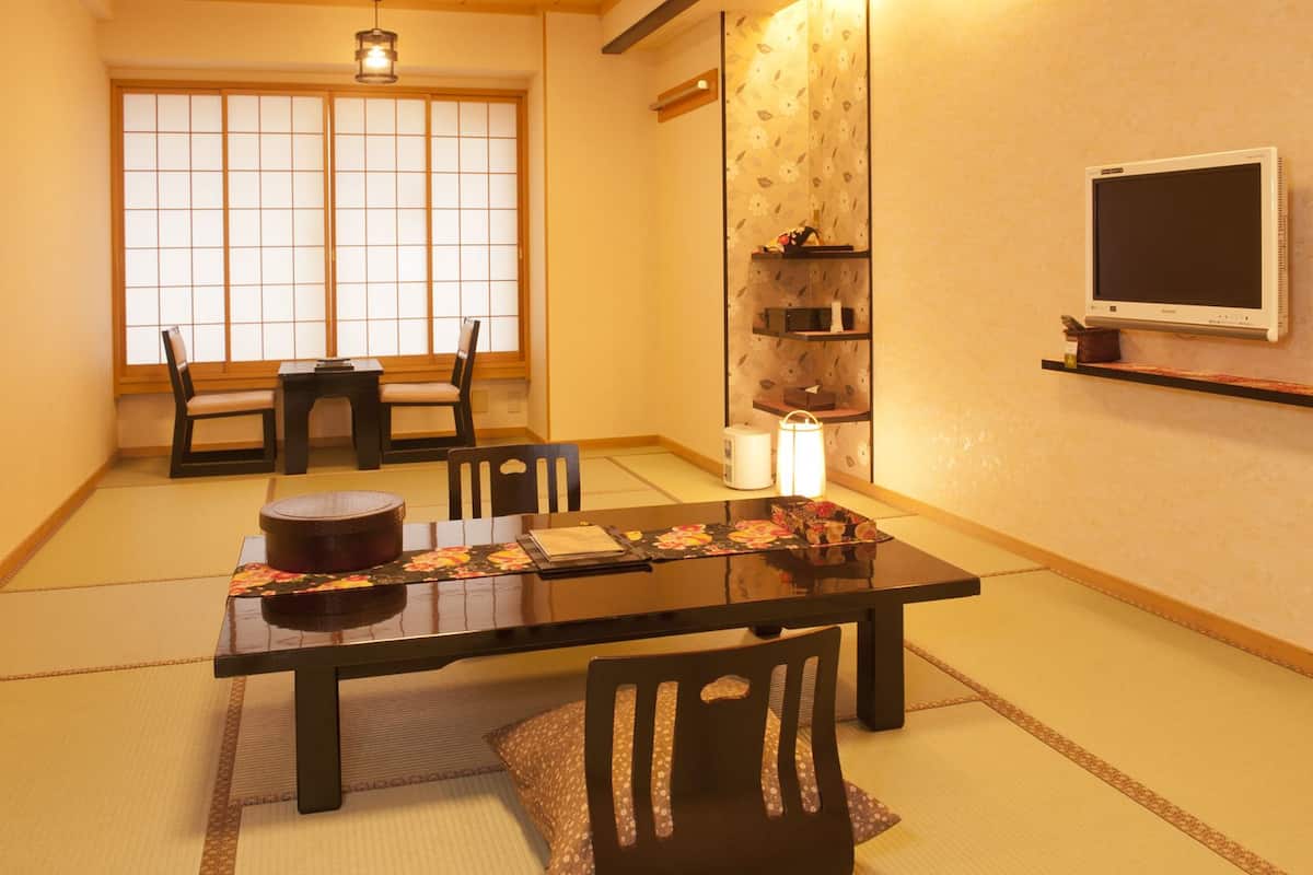 A traditional Japanese room with tatami flooring, a low table with a cushion, a chair, and a shelf with decorative items.
