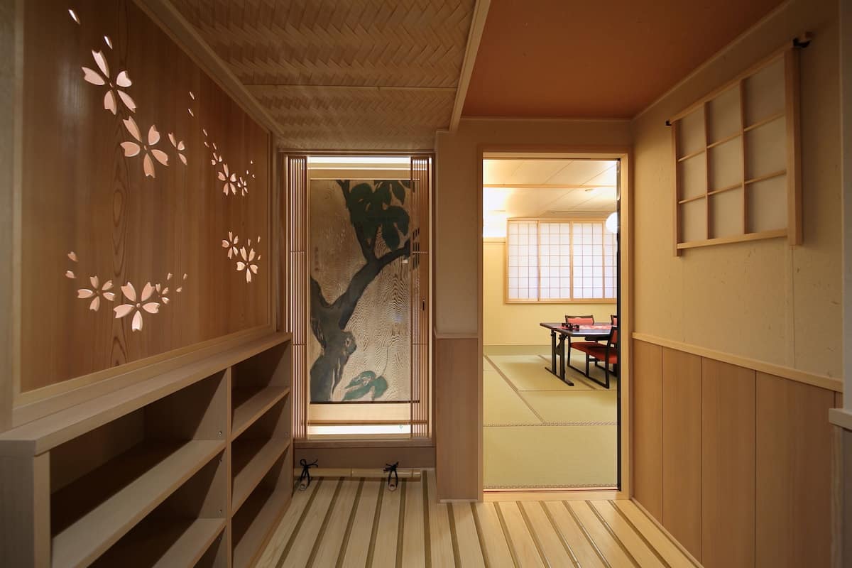 A traditional Japanese room with tatami flooring, a sliding door with a tree design, and a low table with chairs.