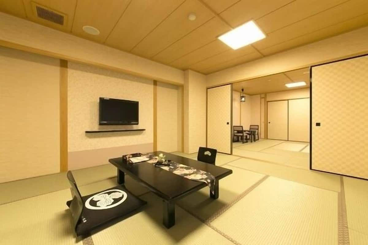 A traditional tatami mat room with a tatami mat table, a television on the wall, and sliding doors leading to another room.