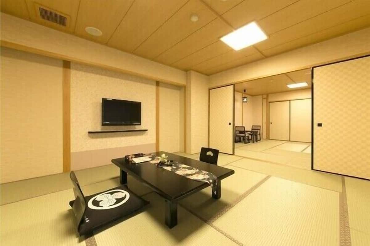 A conference room with tatami flooring, a black table, and a television mounted on the wall.