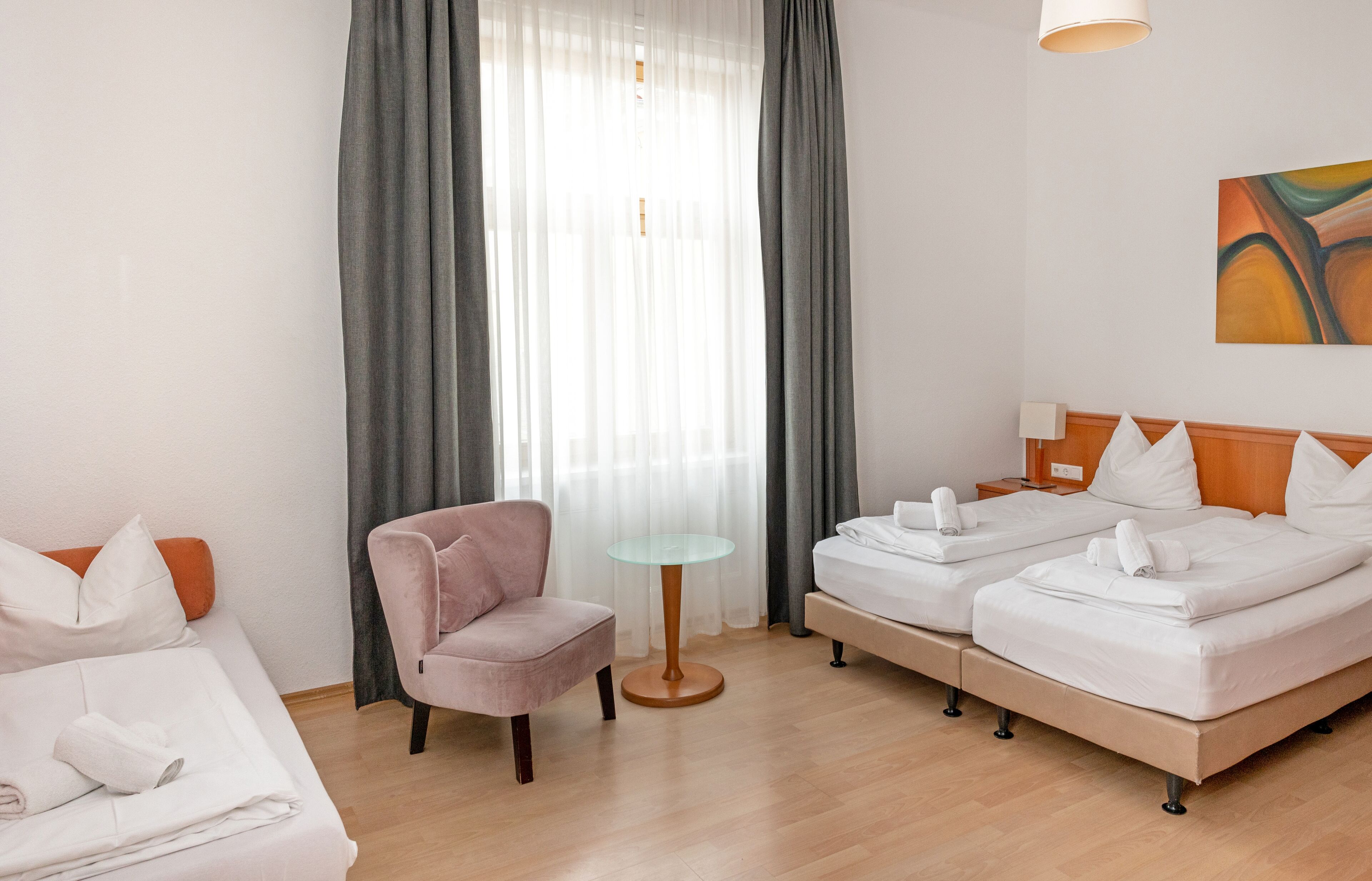 Una habitación de hotel con una cama, una silla, una mesita y un cuadro en la pared.