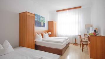 A hotel room with three beds, a desk with a chair, a small table, and a window with curtains.