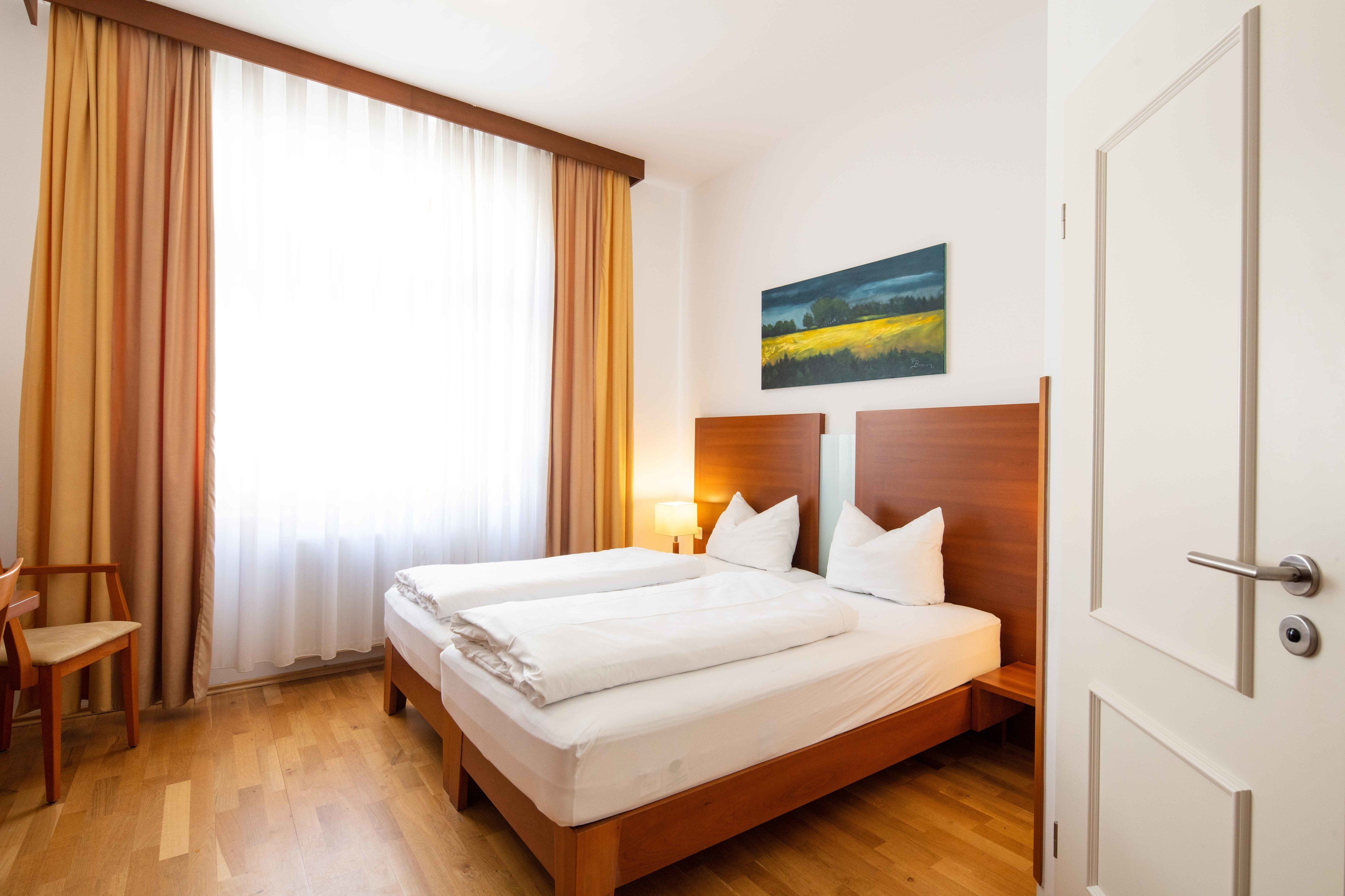 Habitación de hotel con dos camas, suelo de madera, un escritorio y una silla.