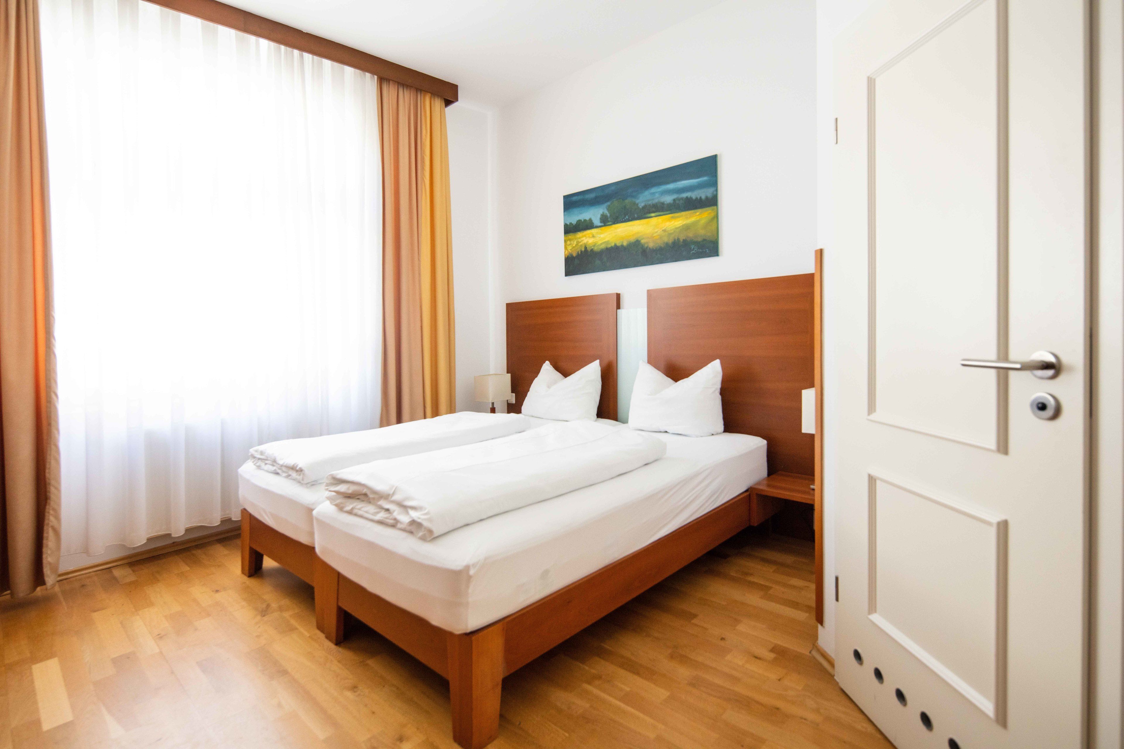A double bed with white linens, a wooden headboard, and a painting above it.