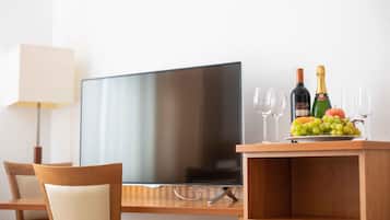 Une chambre d’hôtel équipée d’un téléviseur à écran plat, d’un bureau en bois, d’une lampe et d’une présentation de fruits et de champagne.