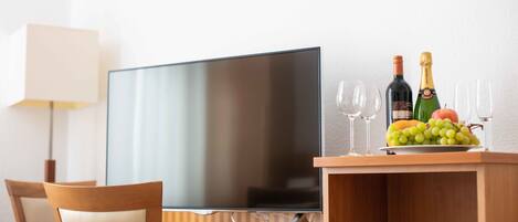 Habitación de hotel con televisión de pantalla plana, escritorio de madera, lámpara y presentación de frutas y champán.