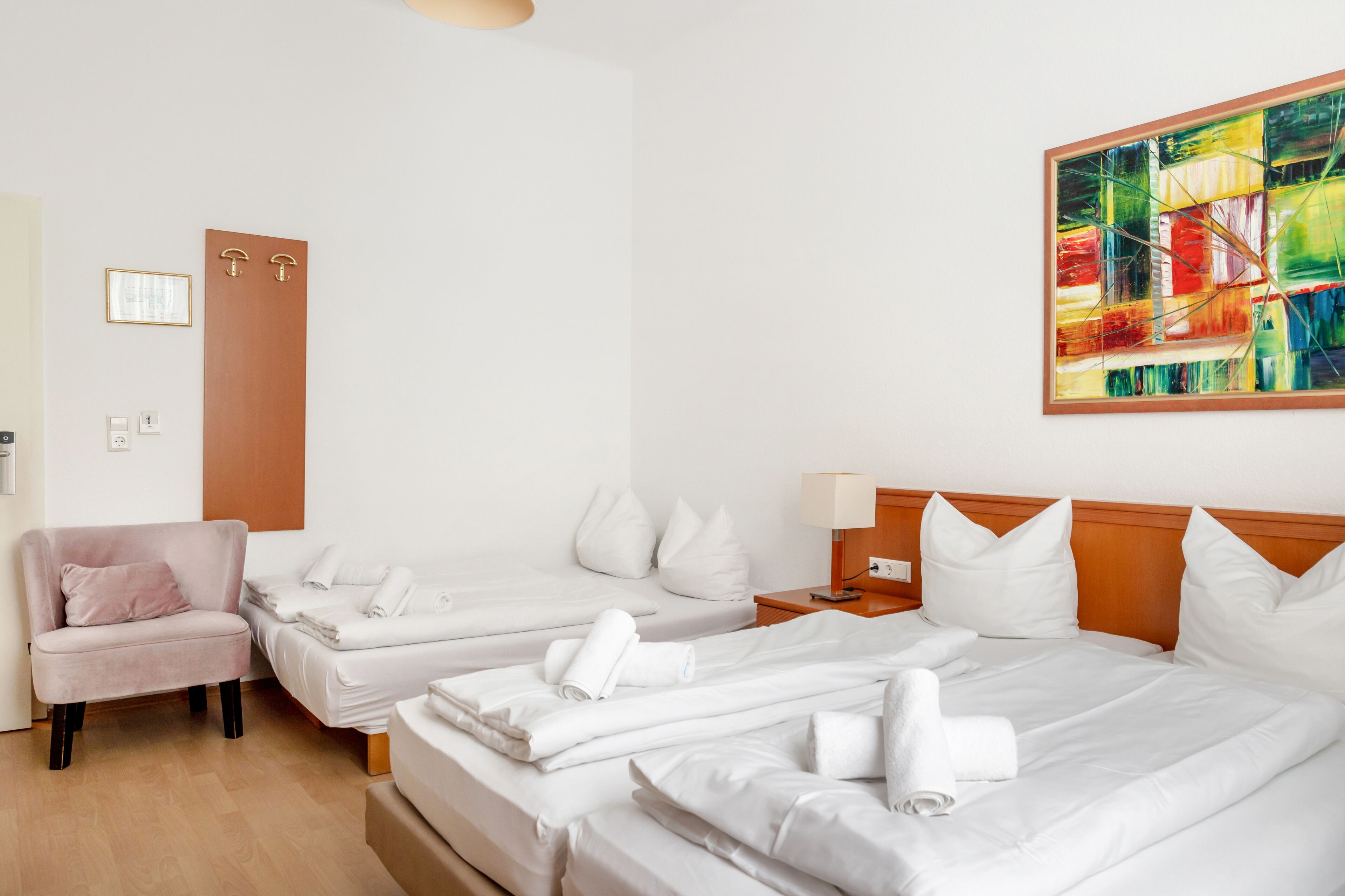 Une chambre d’hôtel avec deux lits, un canapé, une porte en bois, un tableau et une petite table avec une lampe.