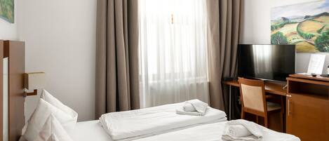 A hotel room with a bed, a desk with a TV, and a painting on the wall.