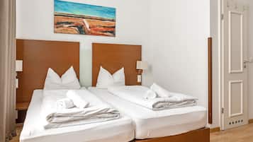 Una cama doble con sábanas y almohadas blancas, un cabecero de madera, una lámpara de noche y un cuadro de un paisaje en la pared.