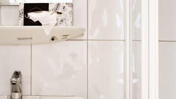 Un baño con un lavamanos blanco, un espejo con luces en forma de rombo y un perchero con toallas blancas.