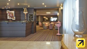 A hotel lobby with a reception desk, seating area, and a large window.