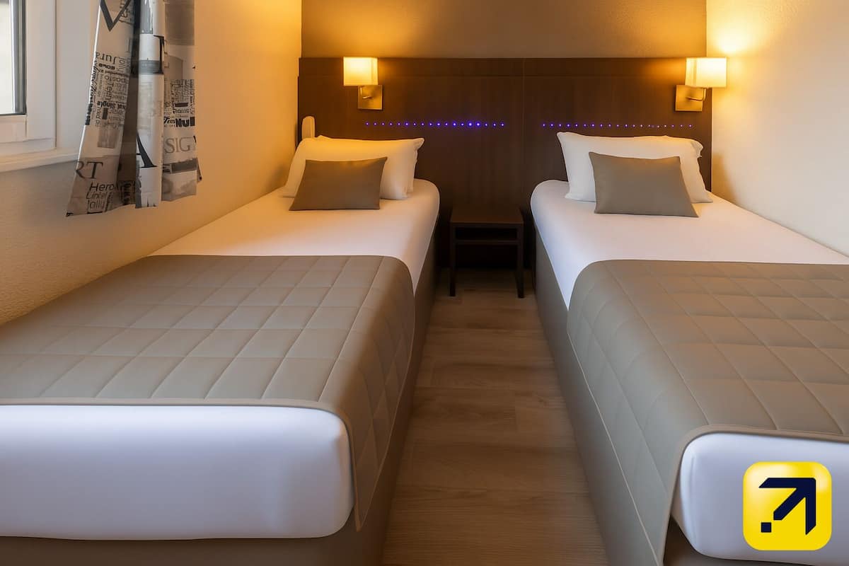 A hotel room with two beds, each with a headboard, bedside lamps, and a small table between them.