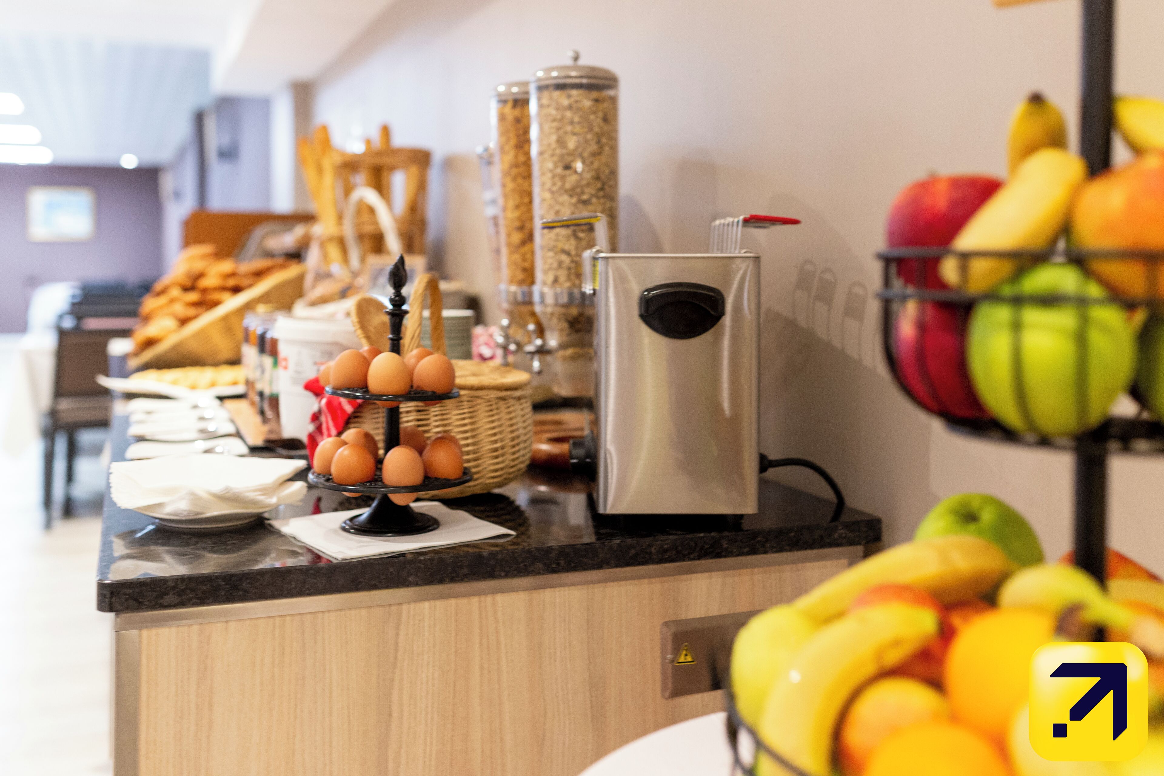 A kitchen counter with a coffee machine, eggs, bread, and a fruit basket.