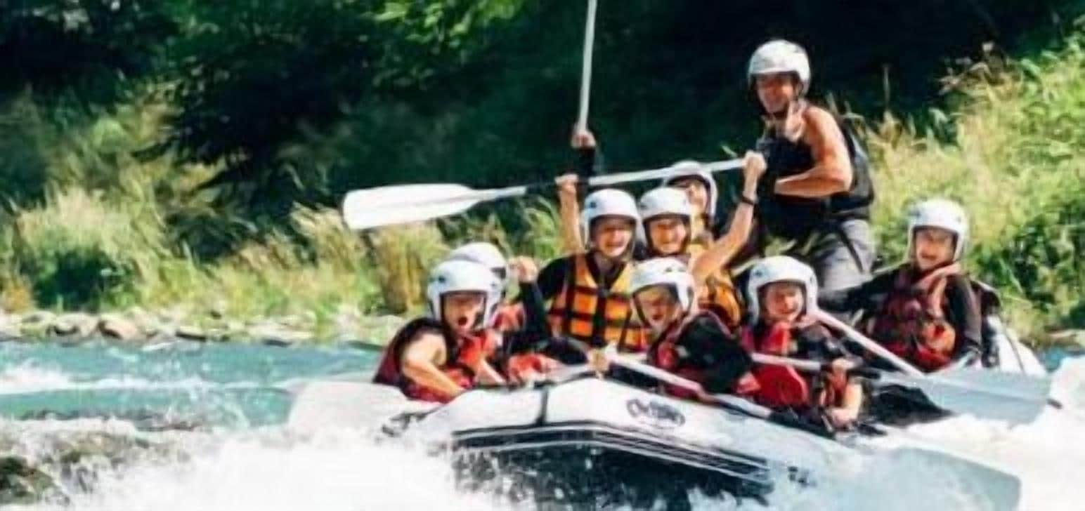 A group of people on a white raft with a paddle, navigating a river surrounded by greenery.