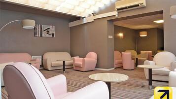 A modern lounge area with sofas and armchairs, a patterned carpet, and a ceiling with a unique light fixture.