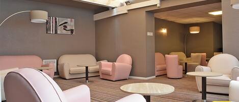 A modern lounge area with sofas and armchairs, a patterned carpet, and a ceiling with a unique light fixture.