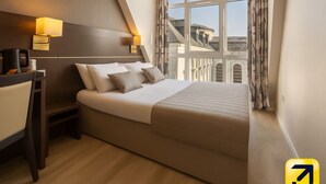 A modern hotel room with a bed, bedside tables, a desk, and a window with curtains.