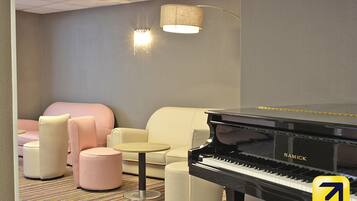 A room with a black Samick piano, a beige sofa, and two pink ottomans.