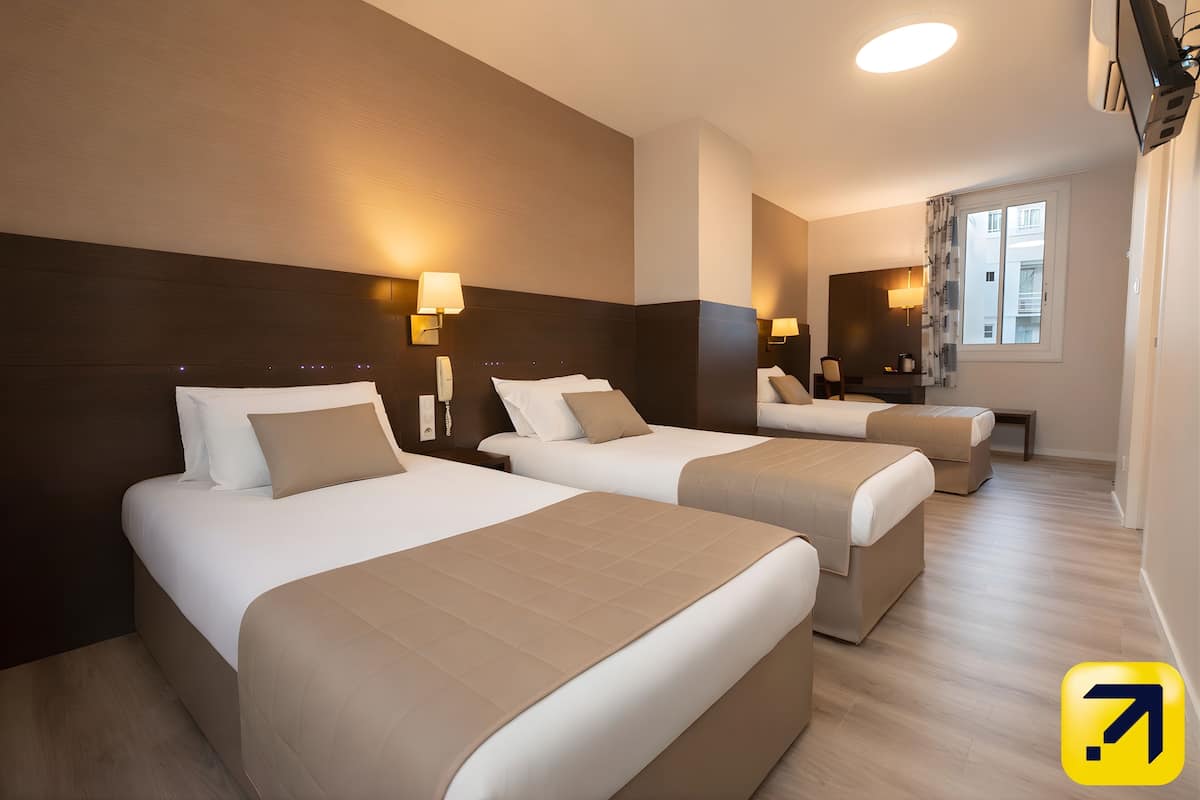 A hotel room with three beds, a desk, and a window.