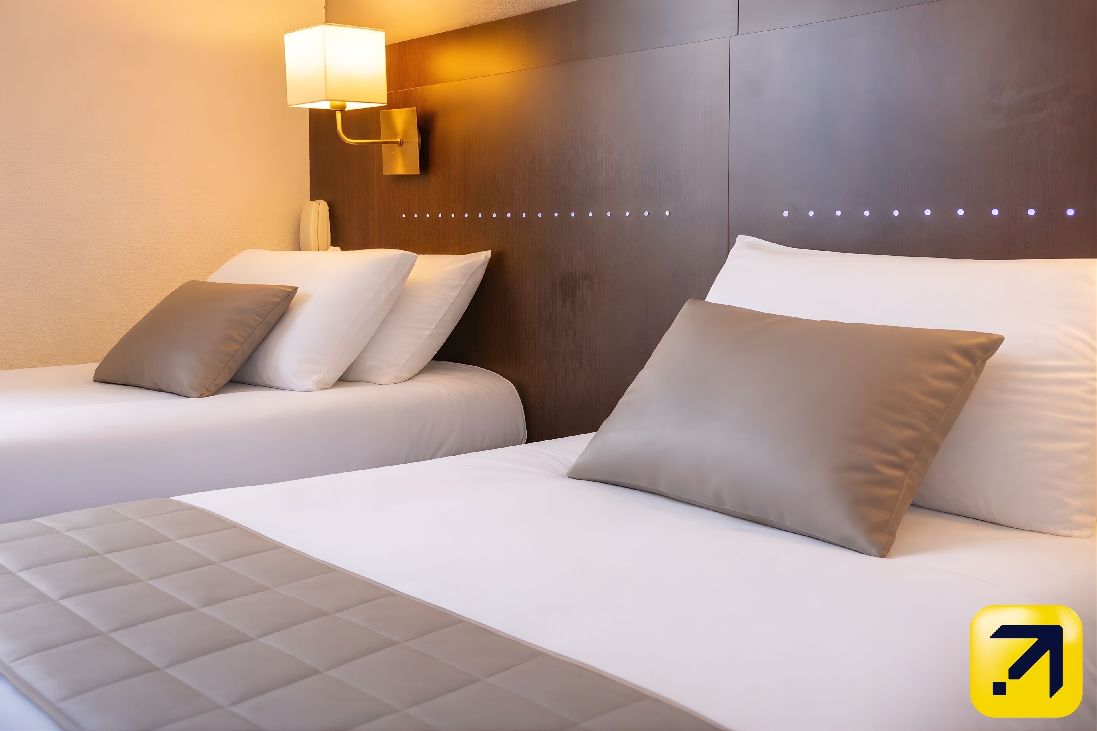 Ein Hotelzimmer mit zwei Betten, einem Nachttisch, einer Lampe und einer Wandleuchte.
