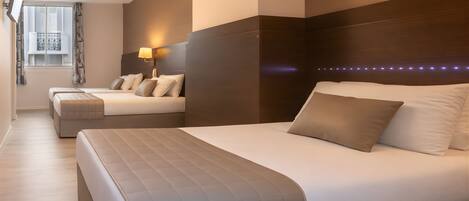 A hotel room with two beds, a TV, a window with curtains, and a wall-mounted lamp.