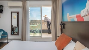 A hotel room with a bed, a desk, a chair, and a balcony with a view. - The Original City, Hotel Cap Maya, Palais des congrès (Agde)