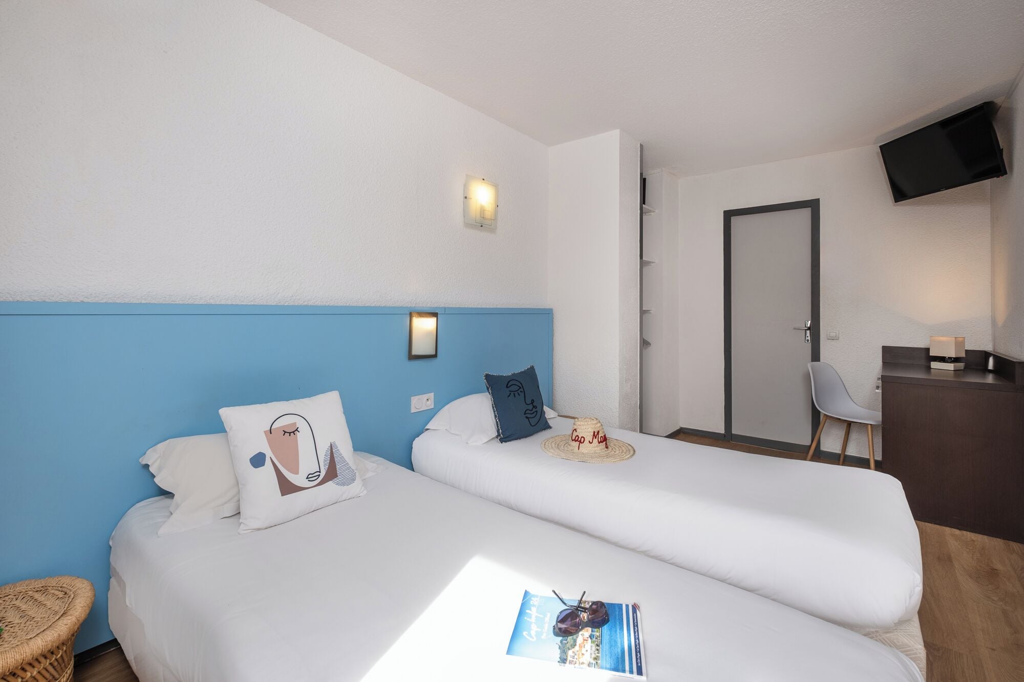 A hotel room with two beds, a desk, a chair, and a TV on the wall.