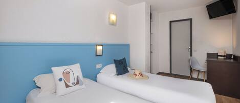 A hotel room with two beds, a desk, a chair, and a TV on the wall.