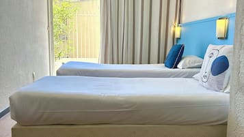 A hotel room with a large bed, a window with curtains, an air conditioning unit, and a view of the outside.