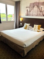 Habitación de hotel con una cama grande, una mesita de noche con lámpara y vista a un muelle de madera a través de la ventana.