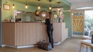 A reception desk with a wooden finish, a mirror, and a framed sign. There are hanging pendant lights and a wall-mounted air conditioner. - The Original City, Hotel Cap Maya, Palais des congrès (Agde)