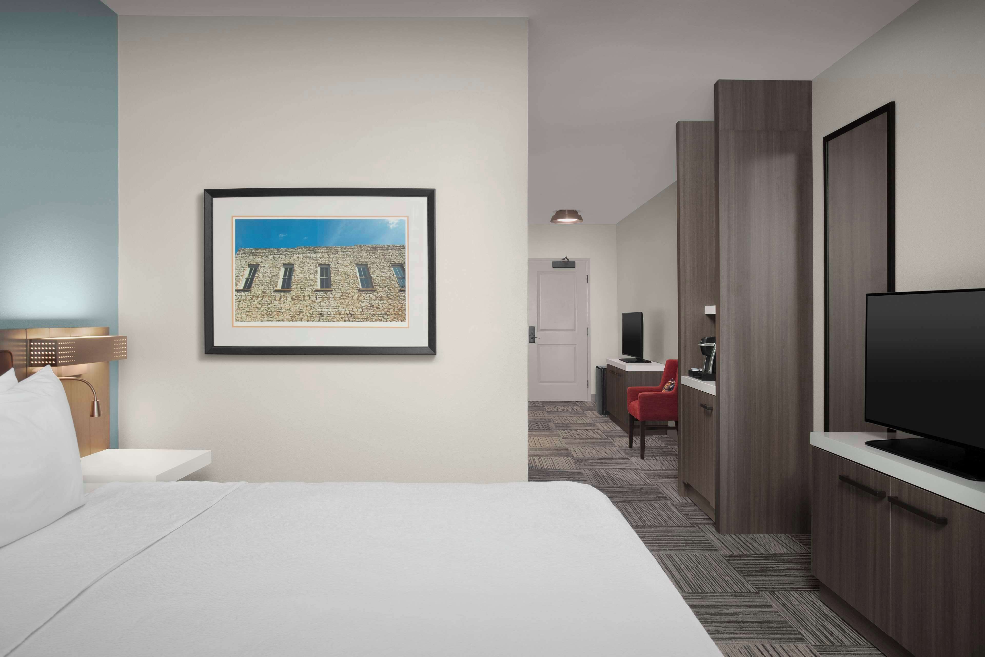 A hotel room with a bed, a framed picture on the wall, a television, and a desk with a chair.