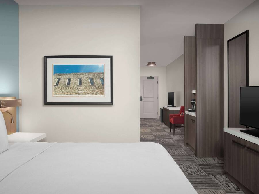 Habitación de hotel con cama, un cuadro en la pared, televisor y escritorio con silla.