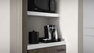 A kitchen with a microwave, coffee maker, and a black container on a white countertop.