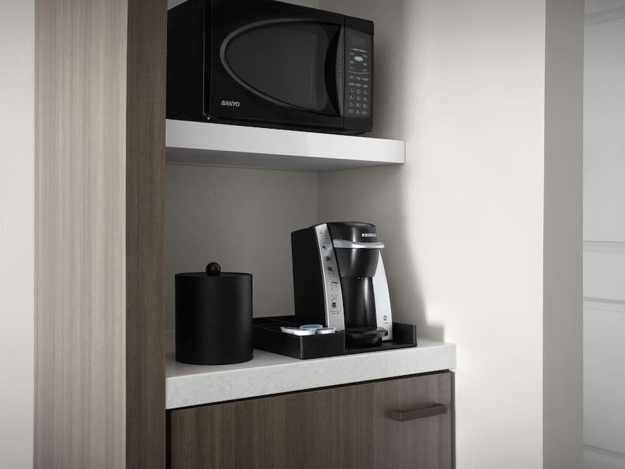 A kitchen with a microwave, coffee maker, and a black container on a white countertop.