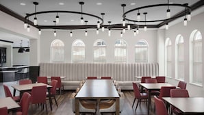 A modern dining area with a long table surrounded by red chairs, a sofa, and a kitchen in the background. - Hilton Garden Inn Granbury (Granbury)